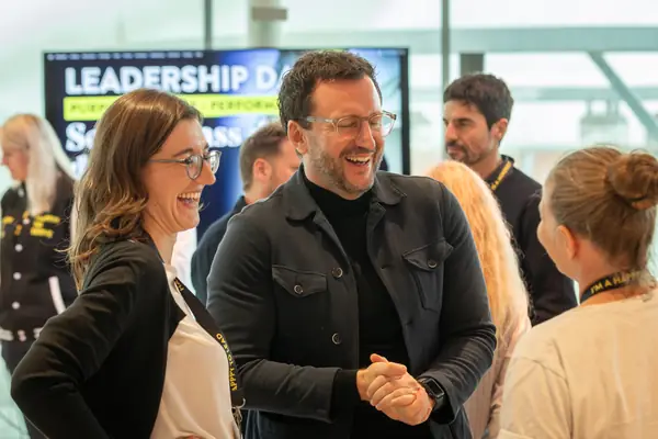 Eine Teilnehmerin mit Brille und ein Teilnehmer in Lederjacke lachen herzhaft vor der Leinwand des Leadership Day