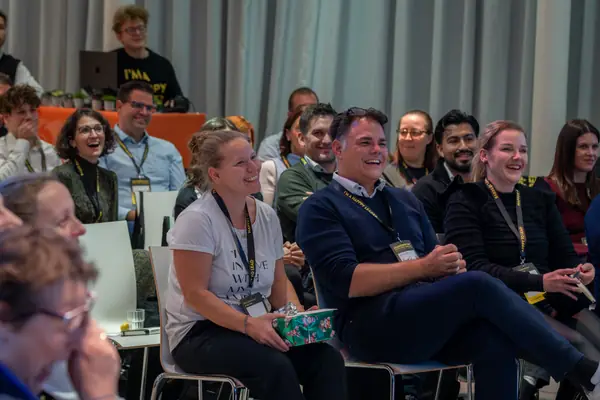 Teilnehmende in mehreren Sitzreihen lachen gemeinsam
