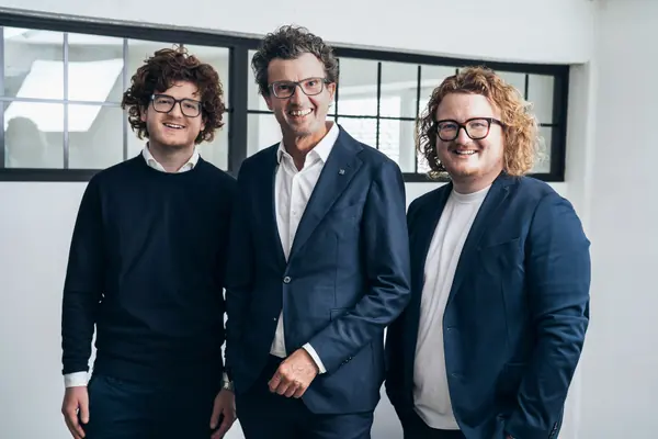 Johannes, Christoph und Maximilian Egger stehen lächelnd nebeneinander vor einer Fensterwand