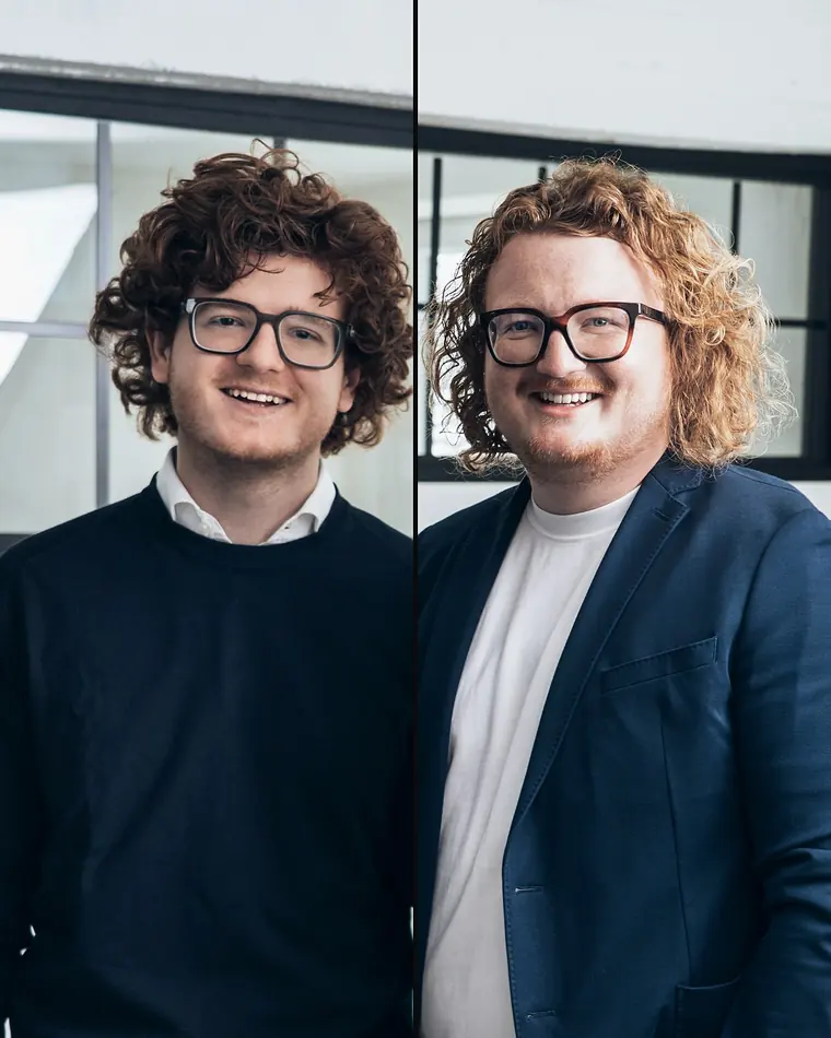 Johannes (links) und Maximilian Egger von gloryfy unbreakable, lächelnd vor einer Fensterwand