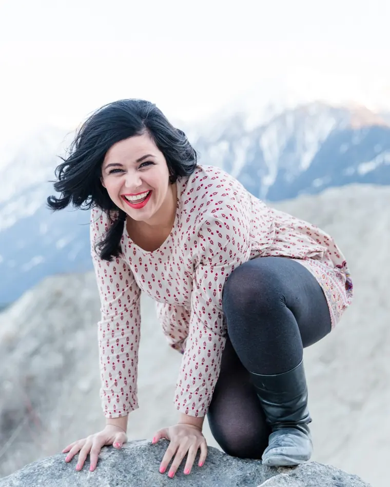 Hannah Philomena Scheiber, lachend auf einem Felsen vor verschneitem Bergpanorama